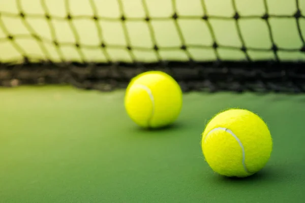 Δυο μπάλες του τένις στο γήπεδο πράσινο, μαύρο συνυφασμένη δίχτυ ως φόντο — Φωτογραφία Αρχείου