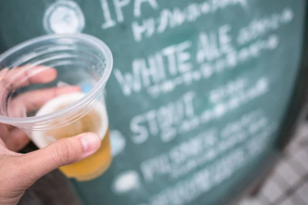 Mano izquierda sosteniendo cerveza artesanal fría en vidrio plástico — Foto de Stock