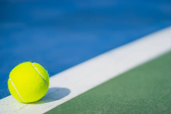 Один новый теннисный мяч на белой линии на сине-зеленом жестком корте со светом слева — стоковое фото
