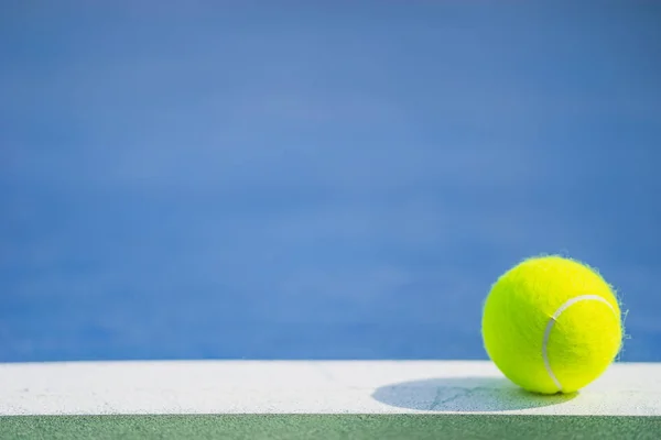 Один новый теннисный мяч на белой линии на сине-зеленом твердом корте со светом справа — стоковое фото