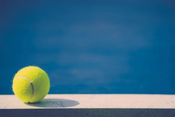 Una nuova palla da tennis su linea bianca in campo duro blu con luce da sinistra — Foto Stock