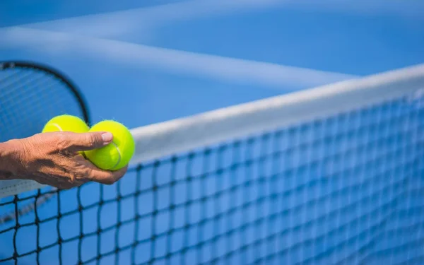 Gammal asiatisk man håller två tennisbollar i höger hand — Stockfoto