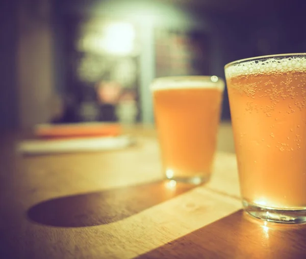 Dos vasos de cerveza artesanal fría con burbujas blancas y sombra sobre mesa de madera — Foto de Stock