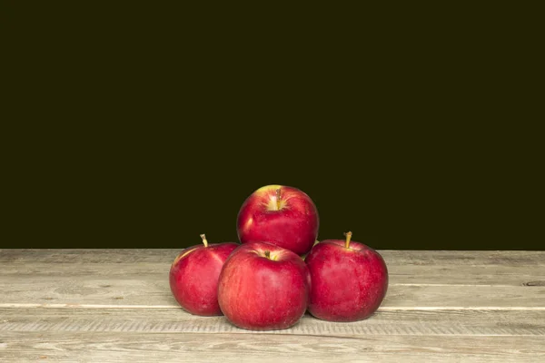four red apples on a wooden table, black background