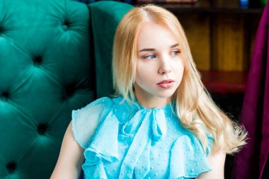 Zarif Bayan kütüphanede penceresine bakarak sandalyede oturan mavi elbise. Güzellik, moda. Doğal ışık stüdyo.