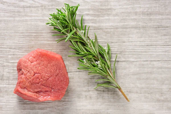 Carne de bovino e alecrim sobre madeira branca ou fundo de pedra — Fotografia de Stock