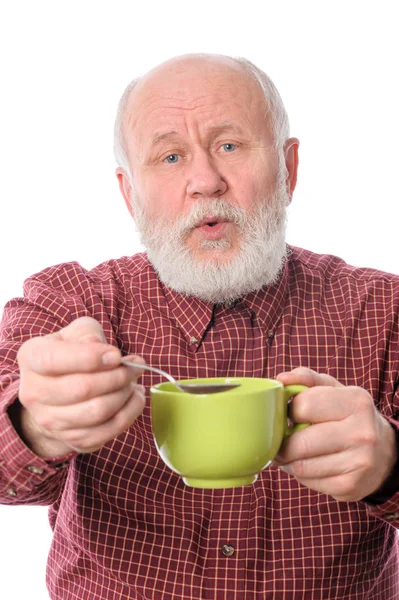 Cheerfull пожилой человек с зеленой чашкой и чайной ложкой, изолированные на белом — стоковое фото