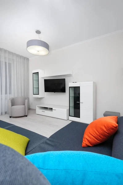 White living room with TV set, chair and grey sofa