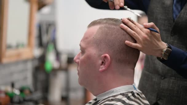 Corte de pelo para hombre en la barbería. Primer plano del maestro cortando a un hombre con el pelo rubio con tijeras — Vídeo de stock