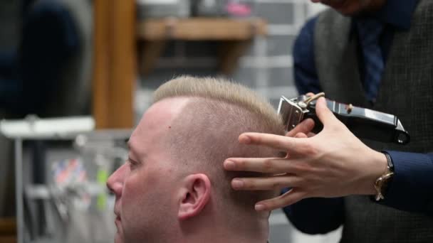 Мужская стрижка в парикмахерской. Крупный план мастера стрижки блондина с клиппером — стоковое видео