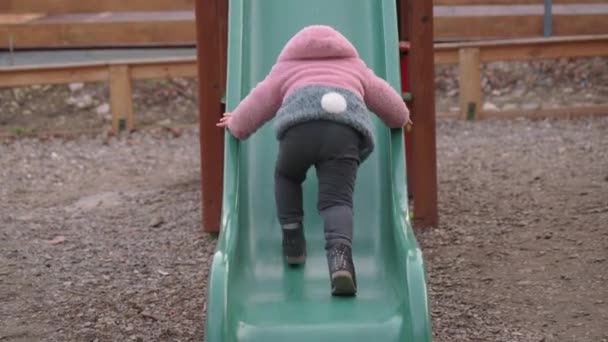 Niña tratando de escalar el tobogán de los niños en el parque infantil local — Vídeos de Stock