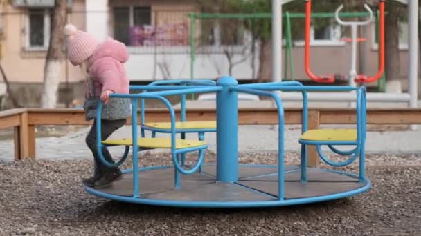 Ensam liten flicka kliver av en karusell på barnens lekplats — Stockvideo