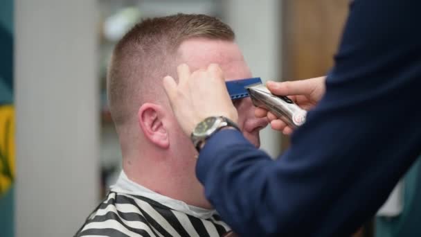 Herrfrisyr i frisörsalongen. Närbild av master klippa en mans panna med clipper och kam — Stockvideo