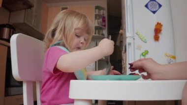 İki yaşında, sarışın, mavi gözlü bir kız yemek yiyor.