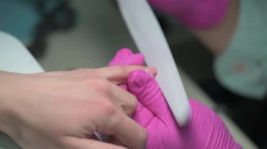 Closeup of manicure beautician prepares clients nails with nail file before covering it with polish