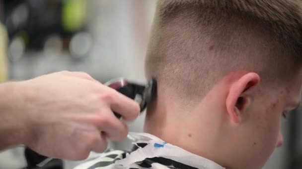 Стрижка молодого человека в парикмахерской. Крупный план мастера стрижки волос с клиппером на затылке — стоковое видео