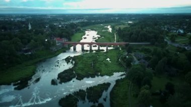 Letonya Kuldiga 'da Avrupa' nın en geniş şelalesinin üzerinde uçmak ve Venta Nehri 'nin karşısındaki tuğla köprü üzerinde güneş doğduktan sonraki akşam uçmak. Areal Dron Vuruşu.