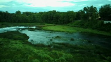 Letonya Kuldiga 'da Avrupa' nın en geniş şelalesinin üzerinde uçmak ve Venta Nehri 'nin karşısındaki tuğla köprü üzerinde güneş doğduktan sonraki akşam uçmak. Areal Dron Vuruşu.