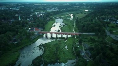 Letonya Kuldiga 'da Avrupa' nın en geniş şelalesinin üzerinde uçmak ve Venta Nehri 'nin karşısındaki tuğla köprü üzerinde güneş doğduktan sonraki akşam uçmak. Areal Dron Vuruşu.