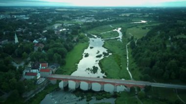 Letonya Kuldiga 'da Avrupa' nın en geniş şelalesinin üzerinde uçmak ve Venta Nehri 'nin karşısındaki tuğla köprü üzerinde güneş doğduktan sonraki akşam uçmak. Areal Dron Vuruşu.
