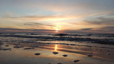 Muhteşem gökyüzü ışığının yansımasıyla Batlic Denizi üzerinde güzel bir gün doğumu. Dalgalar yavaşça sahile vuruyor. Vecaki Plajı Riga, Letonya.