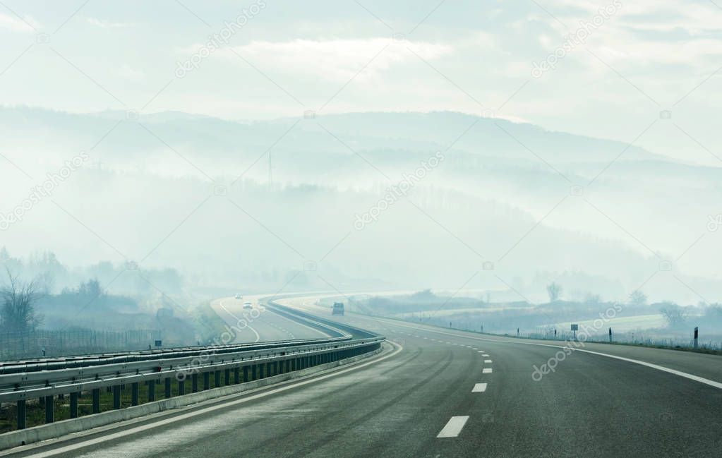Fog over the winding Highway leading to the mountains through the rural landscape
