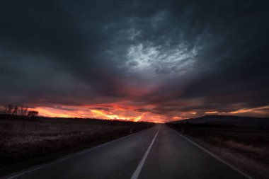 Straight highway road to a dramatic fiery sunset near twilight clipart