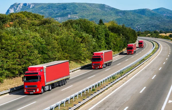 Güzel bir gökyüzünün altındaki bir otoyolda dört kırmızı kamyon konvoyu kuyrukta.