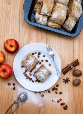 Elmalı turta, Apple Strudel. Elmalı, tarçınlı, cevizli ve kuru üzümlü turta, ahşap bir masada bir tabağa toz şeker serpiştirilmiş.
