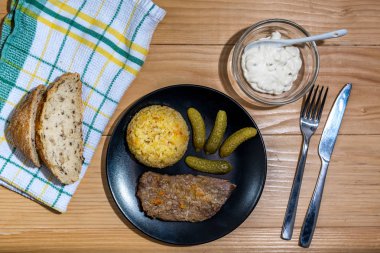 Pirinç pilavlı biftek, turşu ve ahşap masa arkasındaki siyah tabakta sos.