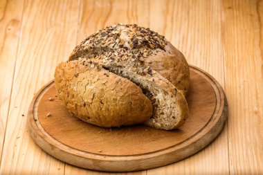 Bir somun buğday ekmeği çeşitli tohumlar serpiştirilmiş, tahta bir masanın üzerinde dilimlenmiş ekmek dilimleri ile.