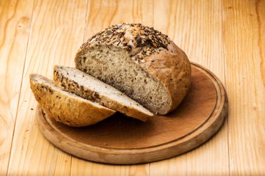 Bir somun buğday ekmeği çeşitli tohumlar serpiştirilmiş, tahta bir masanın üzerinde dilimlenmiş ekmek dilimleri ile.