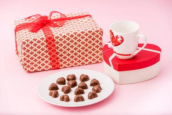 Chocolate Hearts Cookies in a white plate with gift boxes and a coffee cup for Valentine\'s Day on a pink pastel background