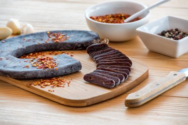 Özel Pirot Nalı Dilimleri ütülenmiş sosis - Dana eti, koyun eti ve keçi etinden yapılmış Peglana Pirotska kobasica, yanında sarımsak, karışık biber, ezilmiş kırmızı biber ve baharatlar, kesme tahtası ve ahşap masa üzerinde