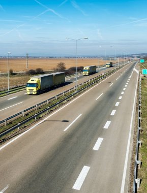 Dramatik bir gökyüzü altında ülke karayolu üzerinde Sarı kamyon karavan veya konvoy