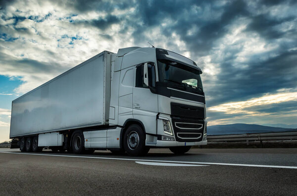 White semi trailer lorry truck on a highway driving at beautiful dramatic sunset. Transportation vehicle