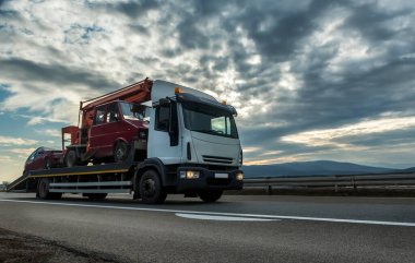 Çekici ya da Flatbed kamyonu dramatik bir gün batımında otoyolda iki aracı çekiyor.