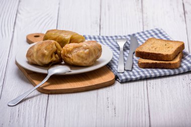 Tahta bir masada beyaz bir tabakta et, pirinç ve sebzeli lahana ruloları. Lahana dolması ve et. Sarma, dolma, Chou farci, golubtsy veya golabki.