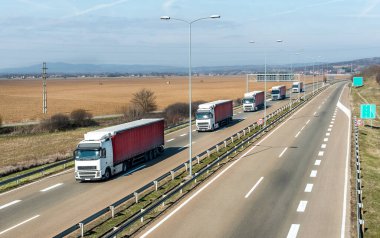 Taşıma kamyonları konvoyu, mavi gökyüzünün altında bir taşra otoyolunda karavan ya da konvoy olarak kuyrukta.