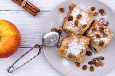 Ev yapımı elmalı turta dilimleri, içinde kırsal beyaz ahşap masa malzemeleri olan bir tabak içinde. Elmalı turta, kuru üzüm ve tarçın, tatlı hamur işleri - Top View
