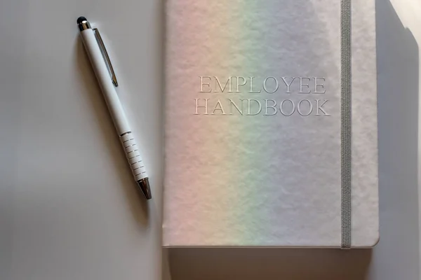 White Employee Handbook or manual with White pen on white surface lit by a light dispersed into rainbow - personnel management policy, explains business goals, results, defines personnel practices