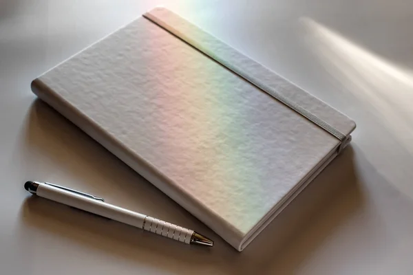 白色的笔记本和笔在白色的表面上被散发出彩虹的光照亮 商业概念 商人的项目 文件的自由篇幅 — 图库照片