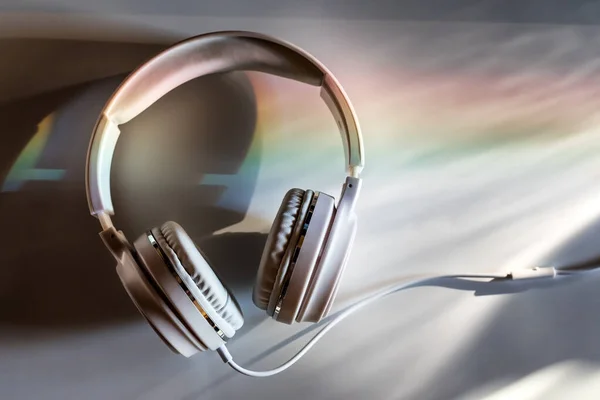 White Headphones On A White table lit by a sunset light dispersed into rainbow. Headphones at the office desk top at the end of the day