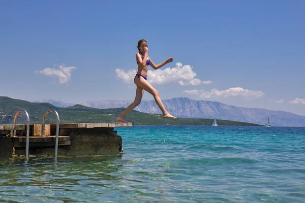 Дівчина стрибає з дерев'яного пірсу в морі — стокове фото