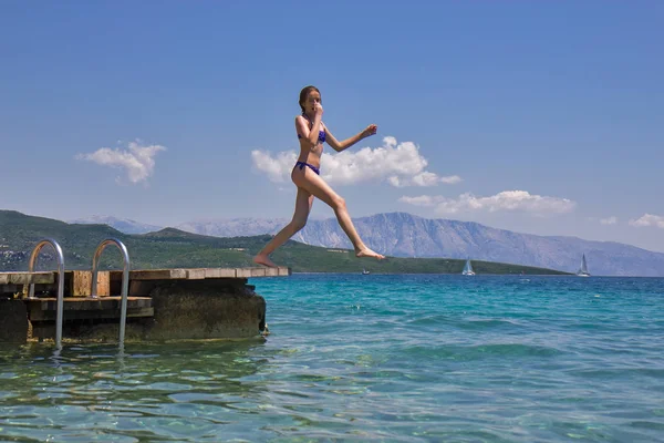 Girl jumping from a wooden pier in the sea — Stock Photo, Image