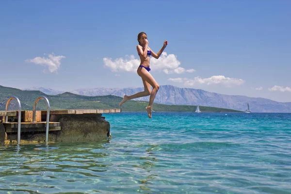Girl jumping from a wooden pier in the sea — Stock Photo, Image