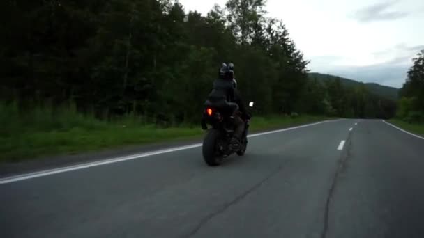 A young biker in a leather jacket and a helmet riding at the motorcycle along the highway around the city. Close-up slow motion — Stock Video