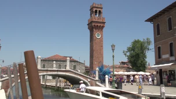 Люди ходят по мосту через башню с часами и стеклянную скульптуру в Мурано — стоковое видео