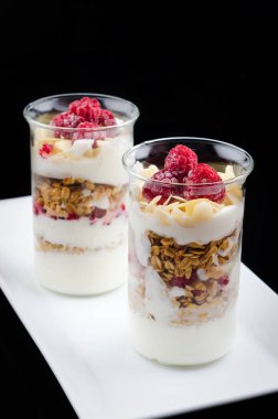 Granola çilek ve beyaz bir tabak ve siyah bir arka plan üzerinde bir bardak yoğurt ile