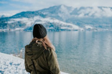 Göl kıyısını arkada karlı dağlar üzerinde duran kadın